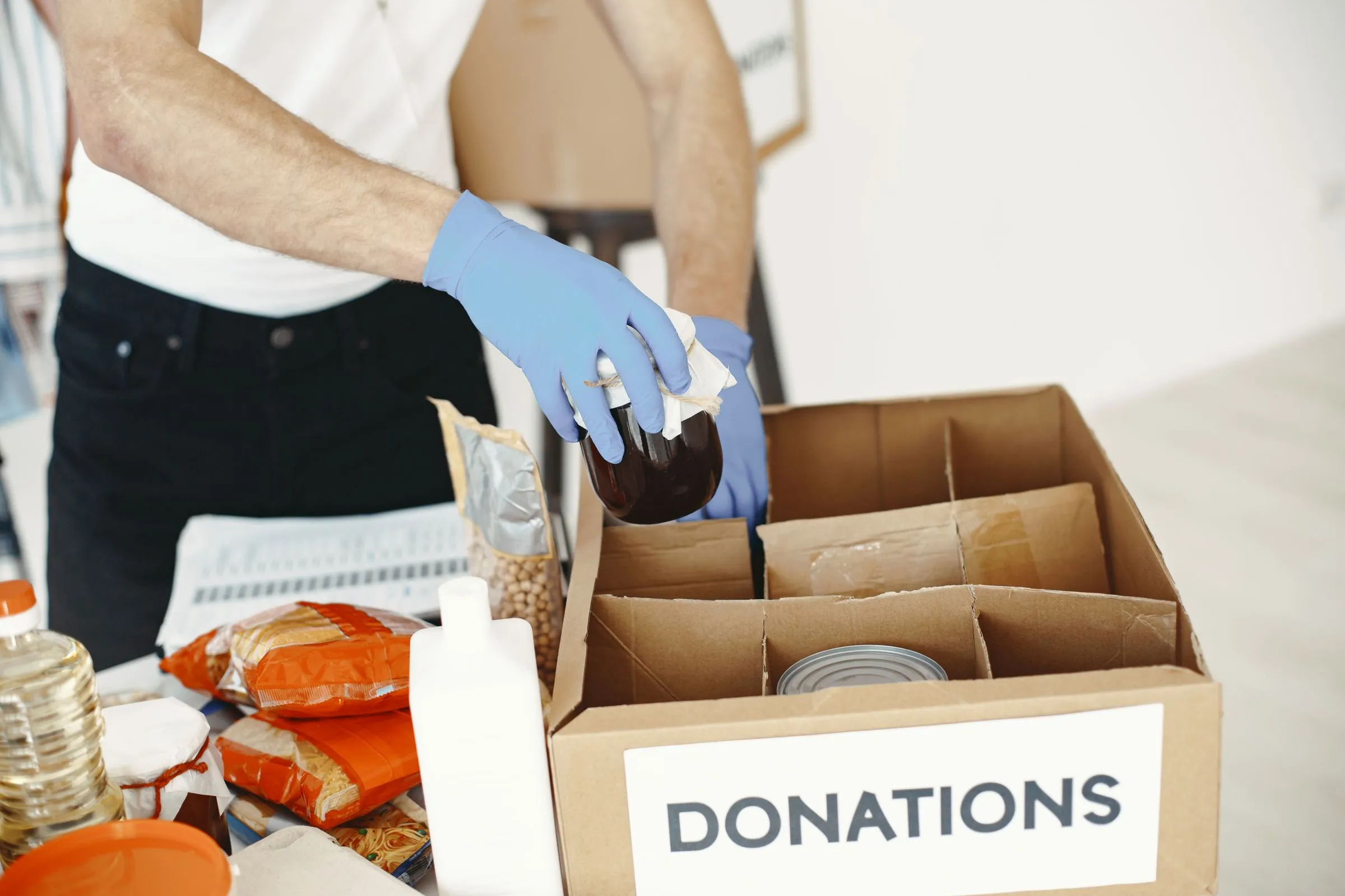 A volunteer in blue gloves packing tins and pasta into a box marked Donations