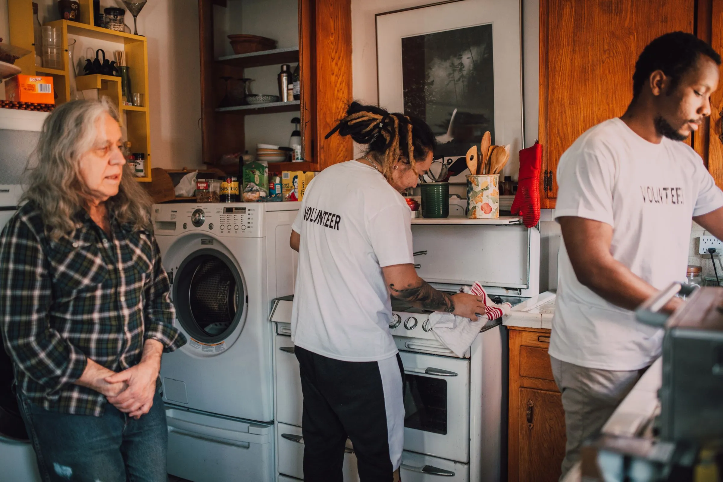 Two volunteers cooking in a neighbour’s kitchen while she looks on